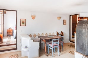 A room with a white sofa, a wooden table, two chairs, a wall-mounted shelf, and a door leading to another room. - Holiday Home 'Can Carabá' with Mountain Views, Private Pool, and Wi-Fi (Sóller)