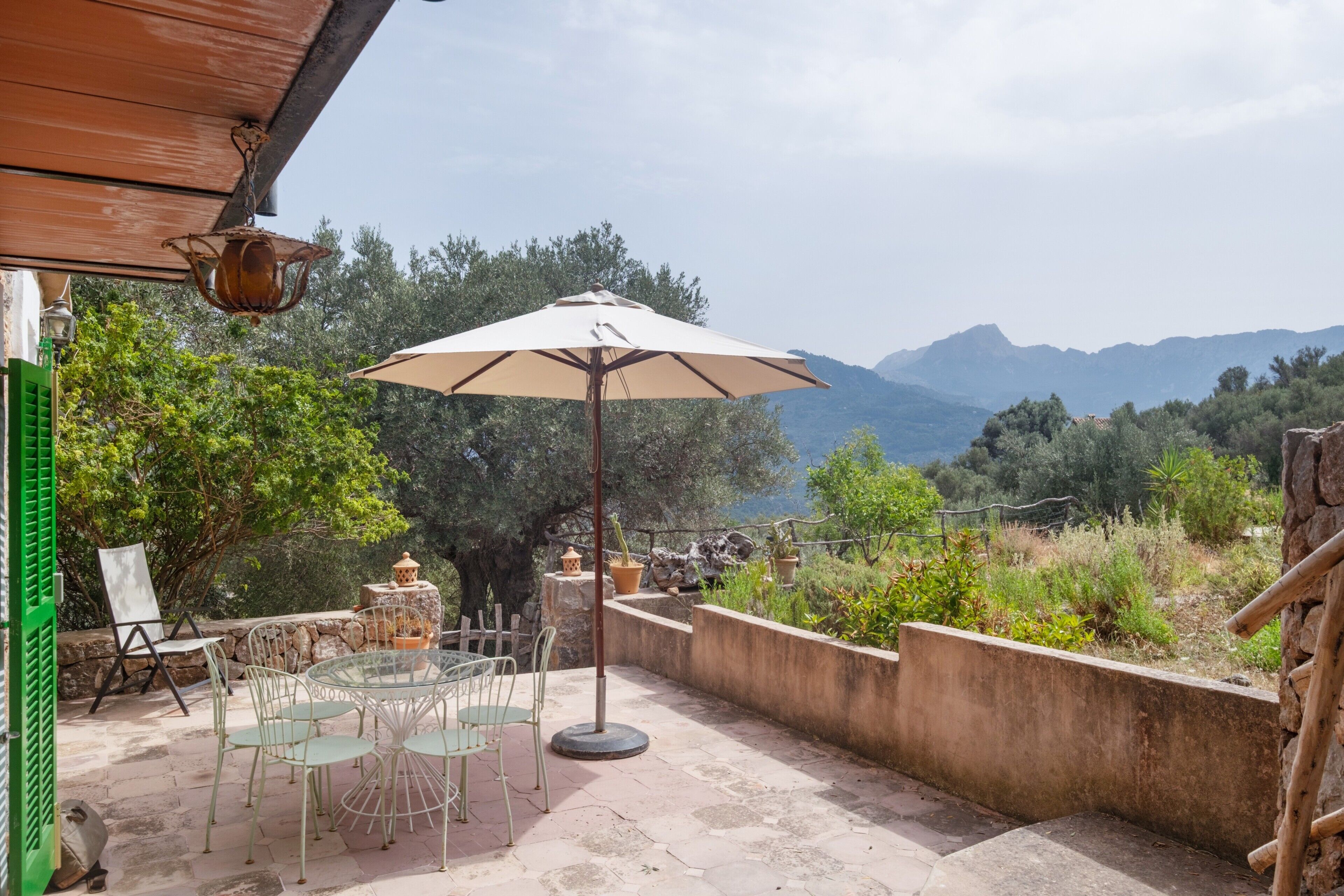 An outdoor patio with a table and chairs, a large umbrella, and a view of mountains.