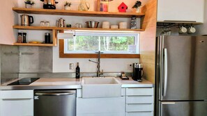 Una cocina con un refrigerador de acero inoxidable, lavavajillas integrado, ventana sobre el fregadero y estantes de madera con diversos utensilios de cocina.