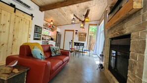 A cozy living room with a red sofa, a fireplace, and a kitchen in the background. - Spa & Sauna | Plume Boreale (Saint-Alexis-des-Monts)