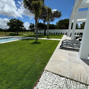 Un espacio exterior moderno con piscina, césped y patio con sillones de descanso.