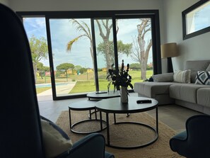 A modern living room with a large sliding glass door leading to a backyard, a round coffee table, a sofa, and a lamp. - PONIENTE BEACH HOUSE New Luxury independent villa 4suite bedroom NovoSancti Petr (Chiclana de la Frontera)