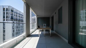 Un balcón con una mesa y sillas, una planta en maceta y vistas de edificios modernos.