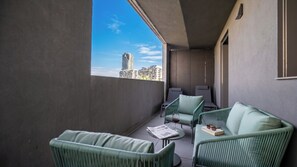 Ein Balkon mit grünen Korbmöbeln, einem Glastisch und einer Zeitung.