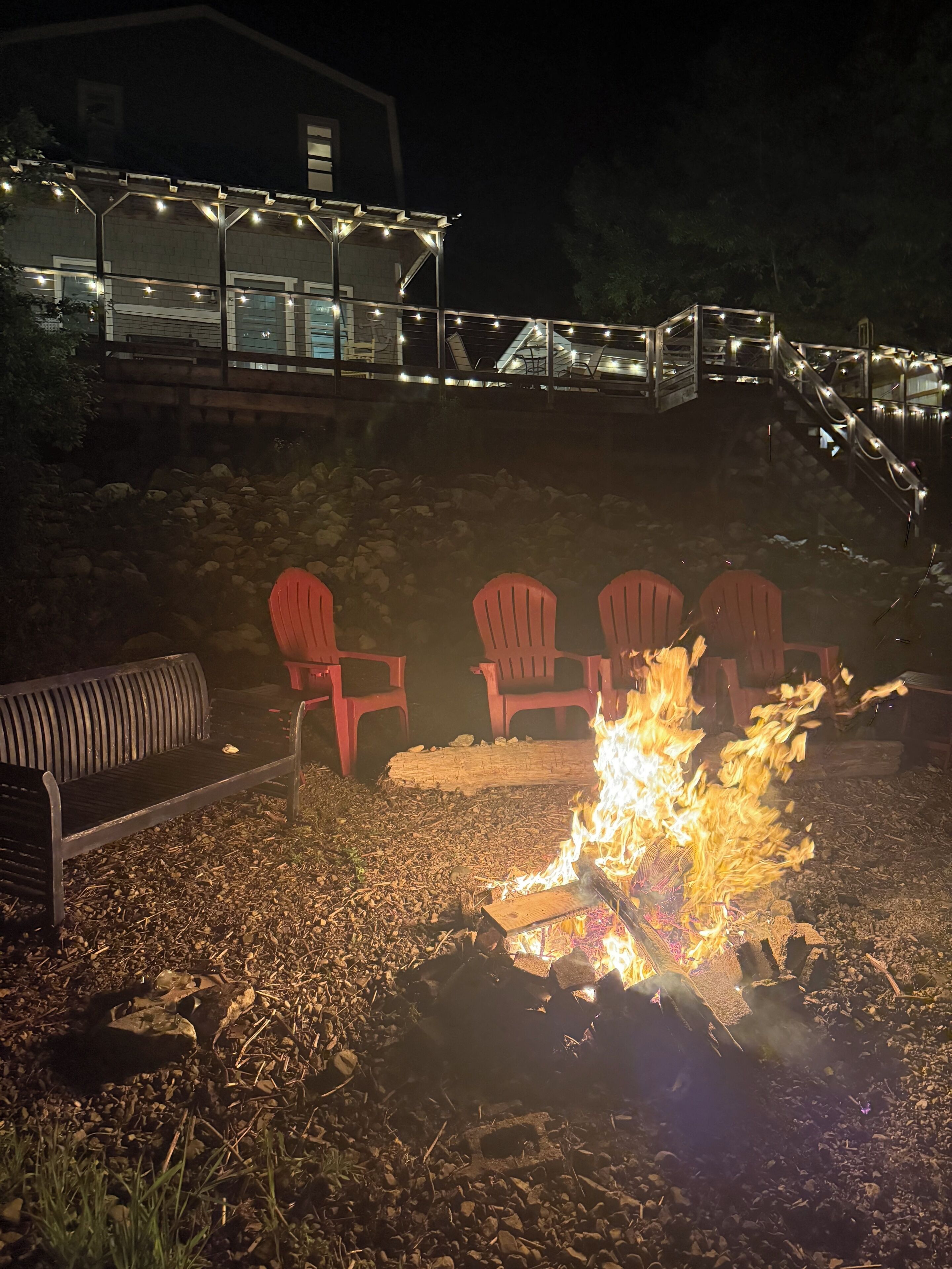 A fire pit with red chairs and a bench, surrounded by gravel.