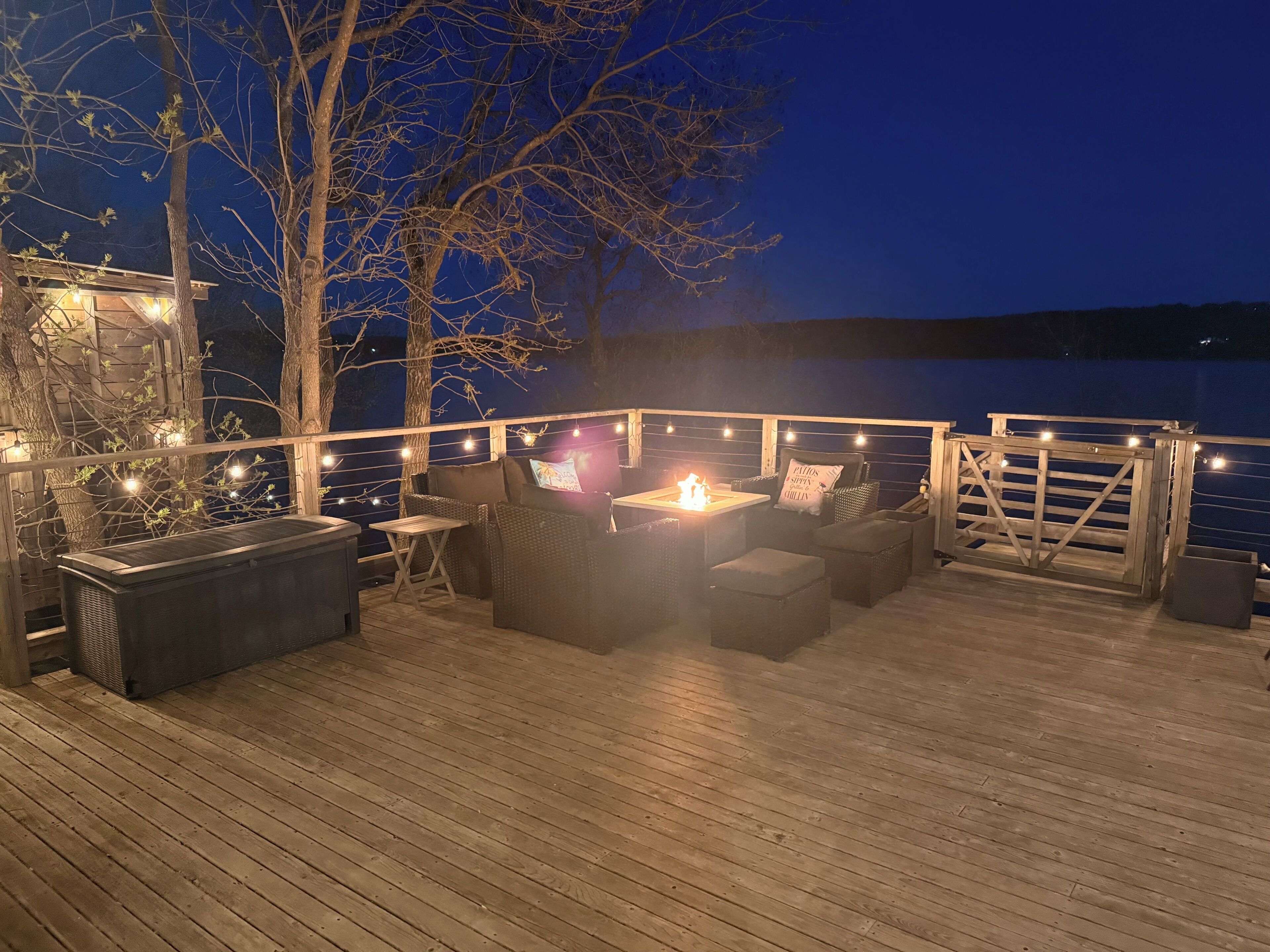 En udendørs terrasse med siddepladser, bålsted og lyskæder.