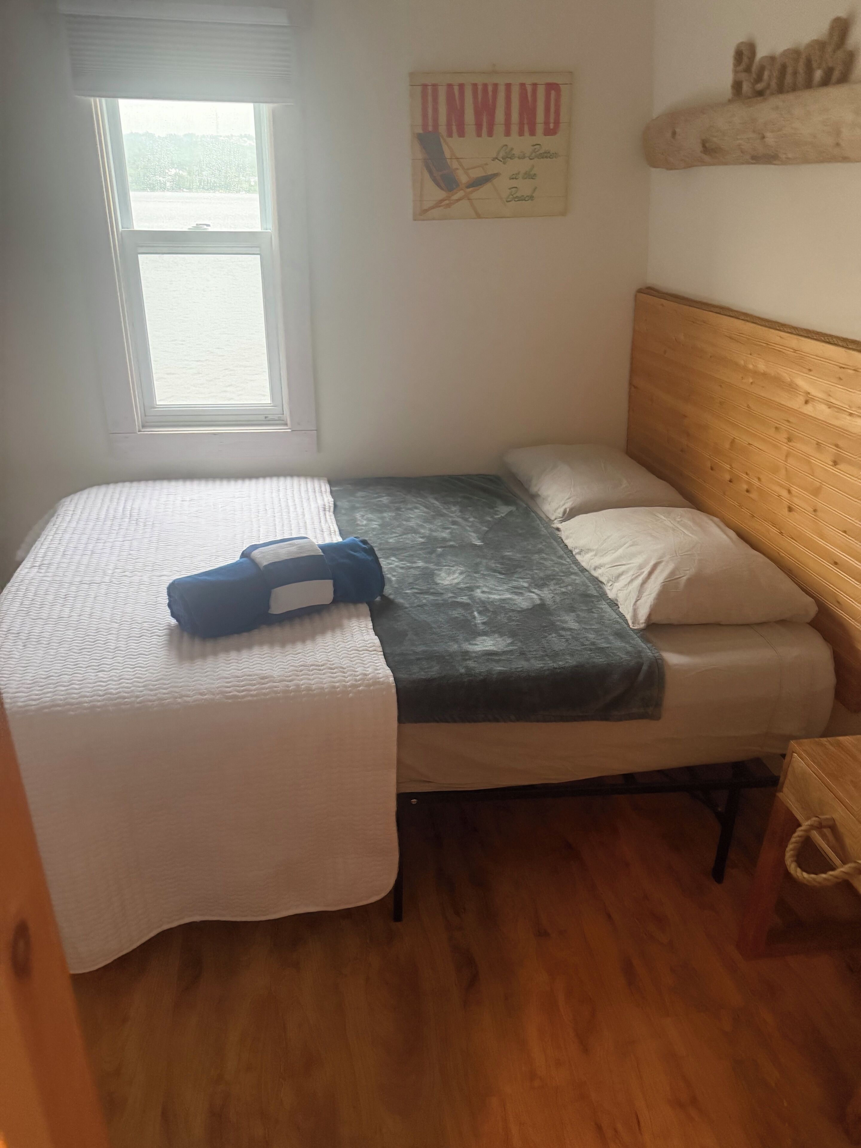 Un dormitorio con cama, ventana, cabecero de madera y un adorno en la pared.