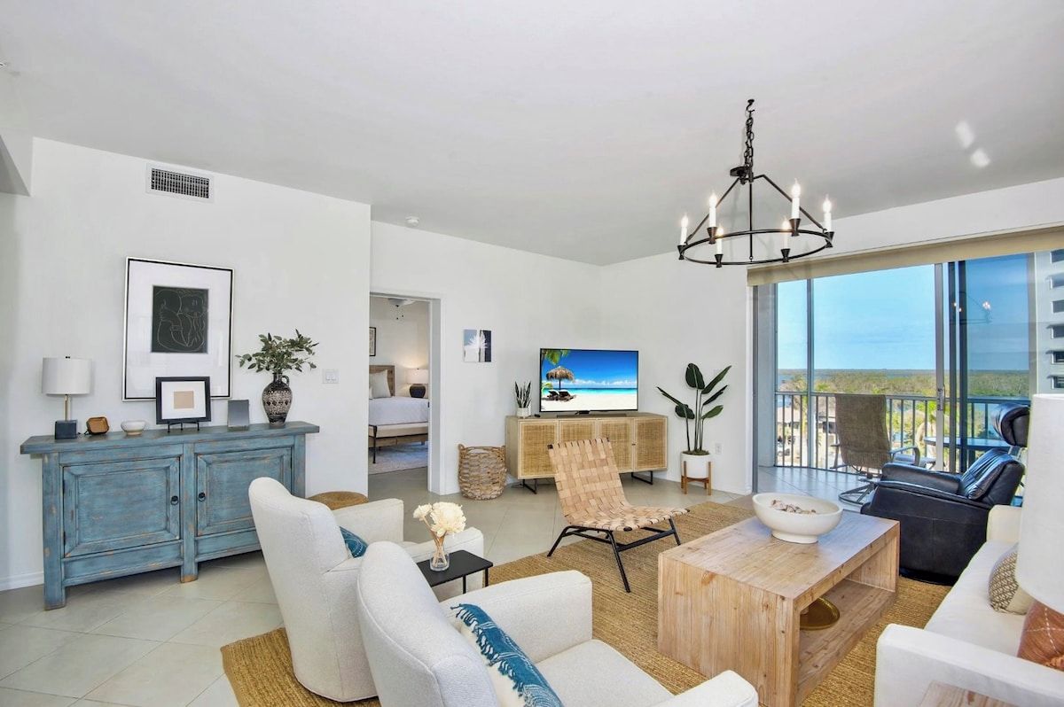 A modern living room with a television, seating, a dining area, and a view of the outdoors.