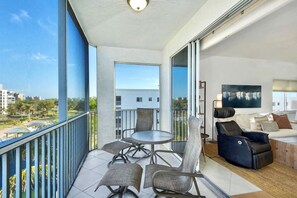 A balcony with a dining set and a reclining chair, a sofa with cushions, and a painting on the wall. - Casa Marina 644 - Bay View (Fort Myers Beach)