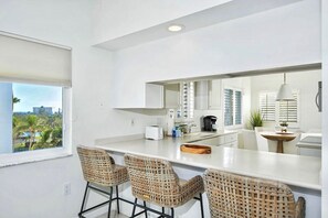 A modern kitchen with a large island, bar stools, and a view of palm trees. - Casa Marina 644 - Bay View (Fort Myers Beach)