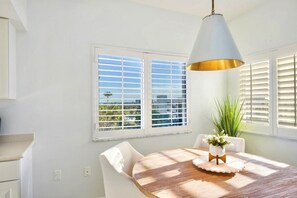 A dining area with a table, chairs, a hanging light fixture, and a window with blinds. - Casa Marina 644 - Bay View (Fort Myers Beach)