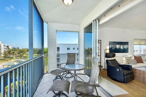A balcony with a dining table and chairs, a sofa, and a TV. - Casa Marina 644 - Bay View (Fort Myers Beach)