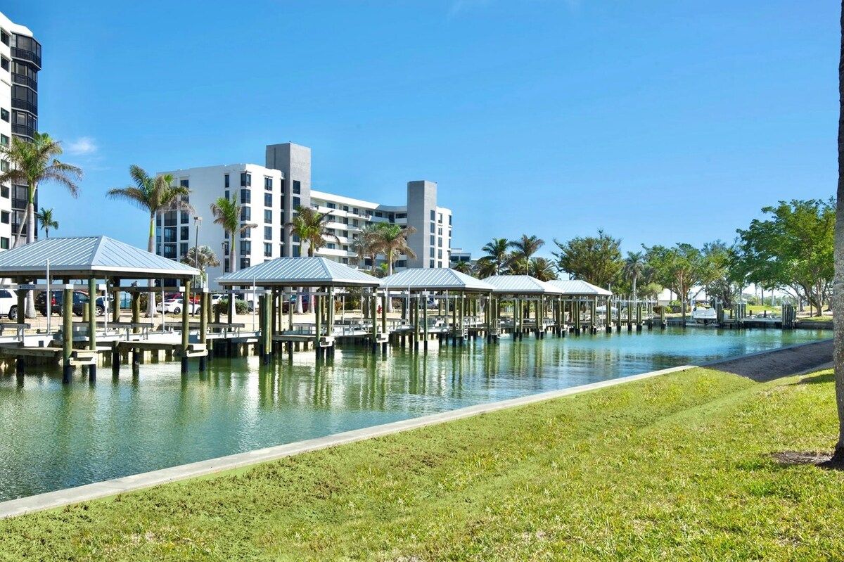 Een hotel aan het water met een zwembad, overdekte doorgangen en moderne gebouwen op de achtergrond.