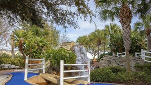 Ein Minigolfplatz mit blauem Putting-Grün, einer Felsformation und einem Wasserfall.