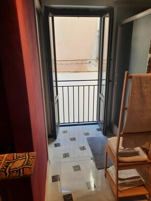 A hallway with a view to a balcony, a wooden chair with a towel, and a patterned table. - 'Centro Casa 2' Studio Apartment – Ideal for Short Stays (Palermo)