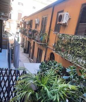 A narrow street with buildings on either side, featuring balconies with plants and outdoor furniture. - 'Centro Casa 2' Studio Apartment – Ideal for Short Stays (Palermo)