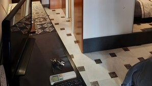 Ett hotellrum med en säng, ett skrivbord med en dator och nycklar, ett inramat konstverk och ett mönstrat golv.