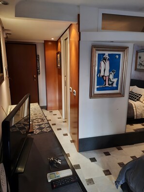 A hotel room with a bed, a desk with a computer and keys, a framed artwork, and a patterned floor. - 'Centro Casa 2' Studio Apartment – Ideal for Short Stays (Palermo)