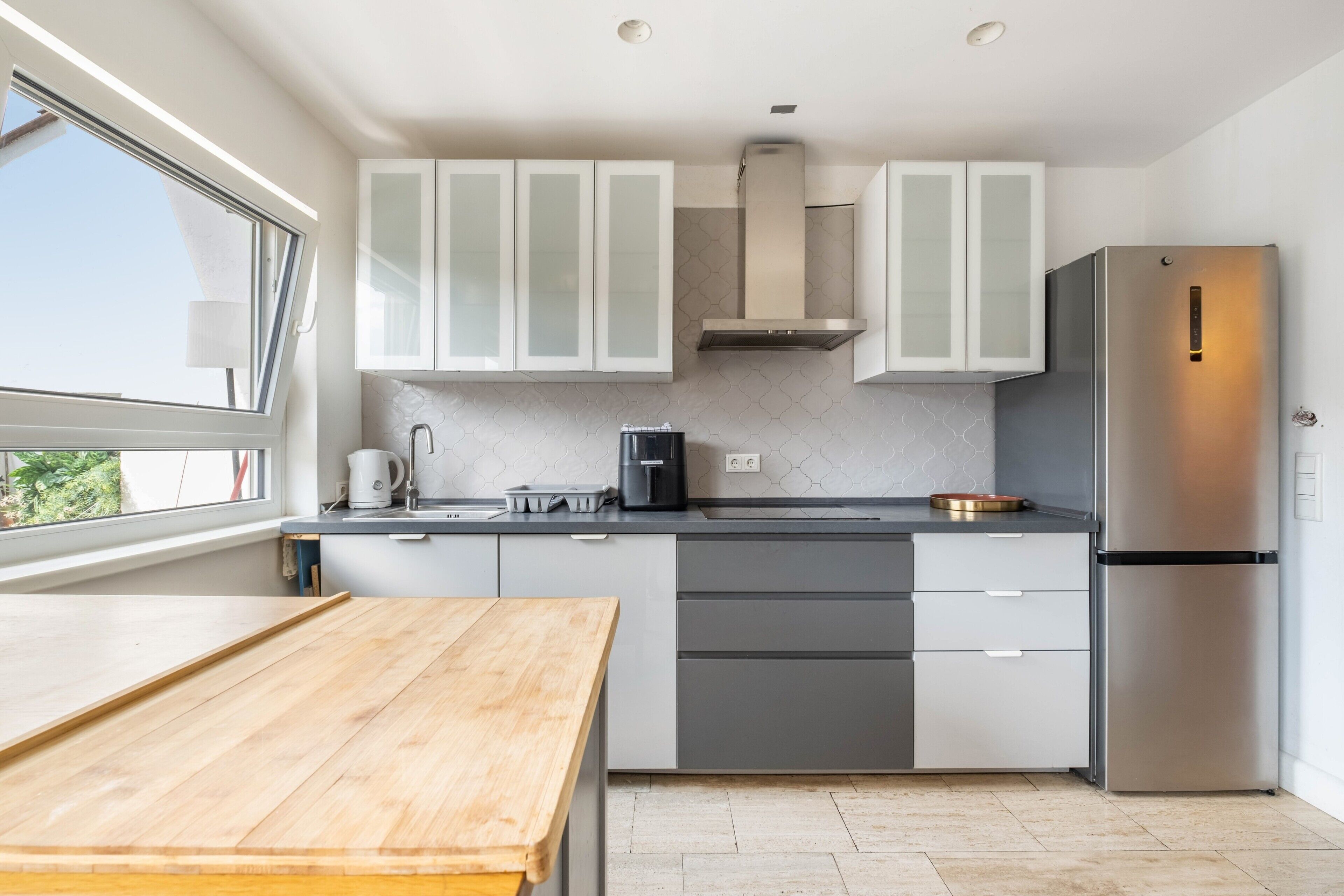 A modern kitchen with white cabinets, a stainless steel refrigerator, and a wooden table.