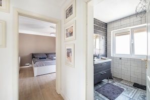 A bedroom with a bed, a bedside table, and a wardrobe. There is a bathroom with a sink, mirror, and a window.