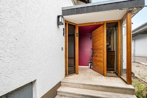 A modern entrance with a wooden door, a red interior wall, and a staircase leading to a covered area.