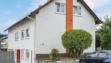 Ein zweigeschossiges Wohngebäude mit weißer Fassade, einer braunen Akzentwand und einem kleinen Baum davor.