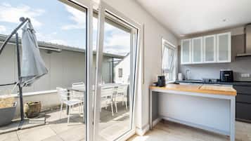 Een moderne keuken met een groot raam, een eethoek met witte stoelen, en een klein terras.
