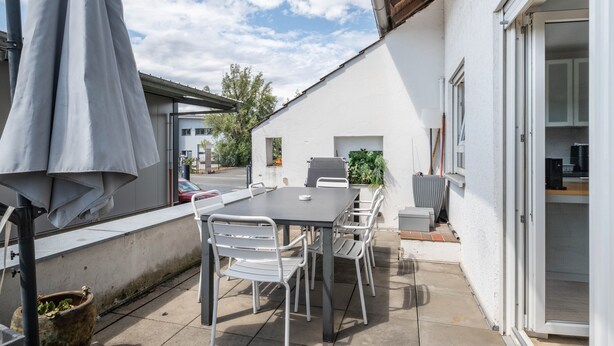 An outdoor patio with a table and chairs, a covered umbrella, and a view of the street.