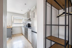 A modern kitchen with white cabinets, a stainless steel refrigerator, and a window with blinds.