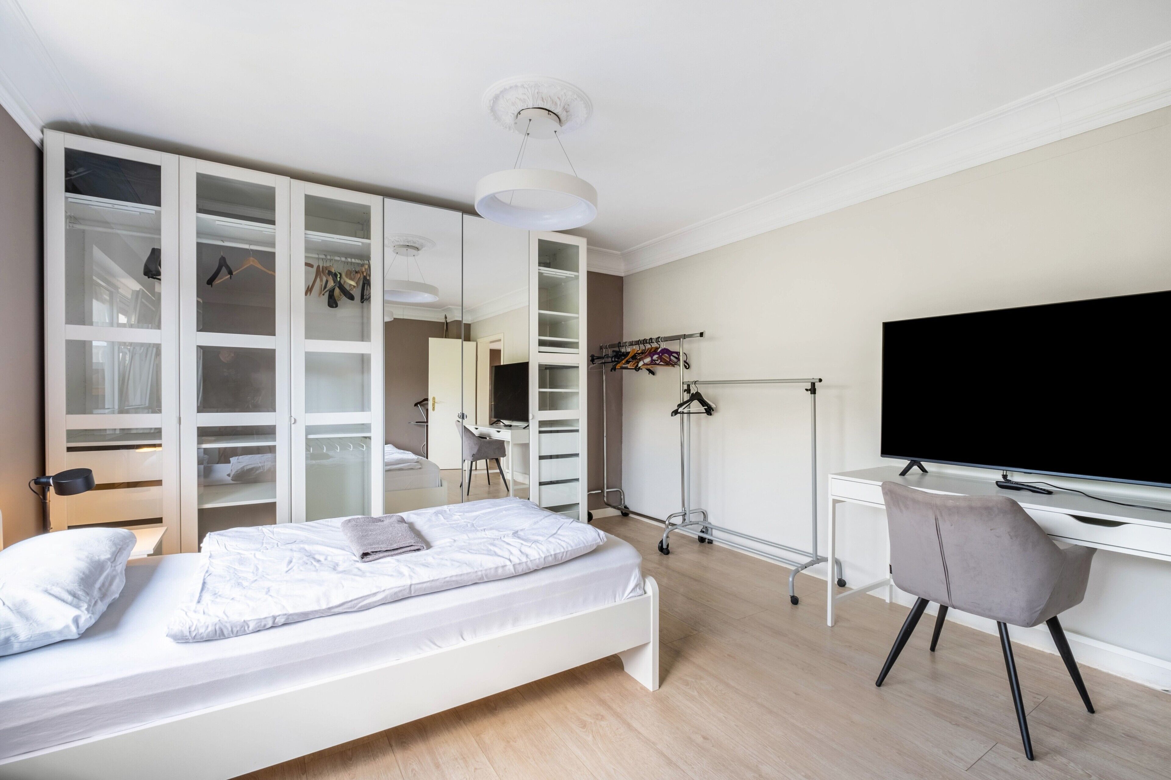 A modern bedroom with a bed, a desk, a chair, a wardrobe, and a television.