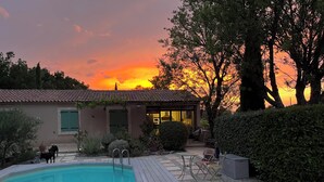 A swimming pool with a tiled deck, a covered patio area, and a building with a tiled roof. - The House Across the Street: A Provençal villa with a pool and air conditioning in Lacoste. (Lacoste)