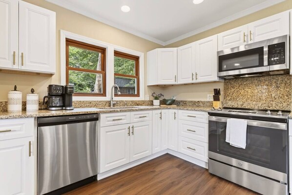A modern kitchen with white cabinets, stainless steel appliances, and a granite countertop.