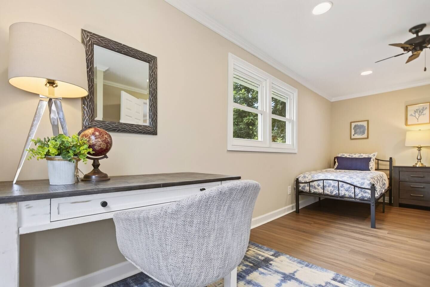 A bedroom with a desk, chair, bed, and a window.