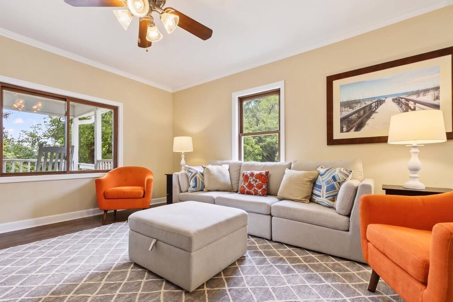 A living room with a sofa, ottoman, two chairs, a ceiling fan, and large windows.