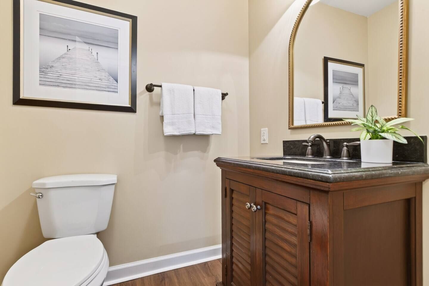 A bathroom with a toilet, a sink with a mirror, and a framed picture on the wall.