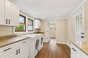 A laundry room with built-in washers and dryers, white cabinetry, and a wooden floor. - Renovated 3BR near Lake Keowee & Clemson (Seneca)