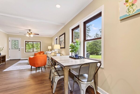 A dining area with a wooden table and metal chairs, a ceiling fan, and a view of the outdoors through large windows.