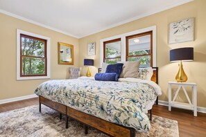A bedroom with a large bed, two bedside lamps, a window, and a framed picture on the wall.