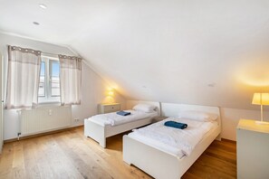 A bedroom with two single beds, a radiator, a window with curtains, and a nightstand with a lamp.