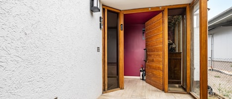 Een moderne ingang met een houten deur, een rode binnenmuur en een trap naar een overdekt gebied.