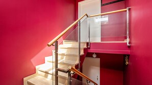 Una escalera con barandillas de vidrio y pasamanos de madera, que conduce a un rellano con una puerta.