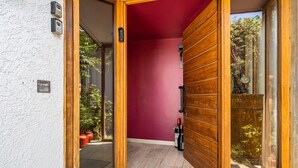 Una entrada moderna con puerta de madera, pared roja y puerta de cristal que da a un patio con plantas en macetas.