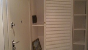 Een kamer met een witte deur, een klein plankje, een lijst met een afbeelding en een inbouwkast met planken.