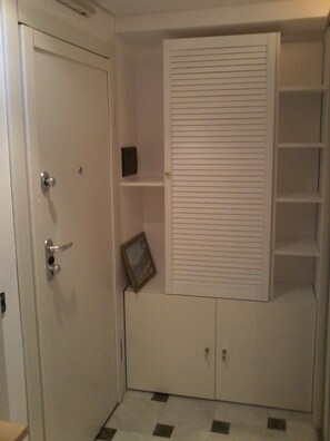 Ein Zimmer mit weißer Tür, einem kleinen Regal, einem gerahmten Bild und einem Einbauschrank mit Regalen.