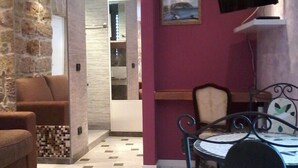 Een woonkamer met een bank, een eettafel met stoelen, een aan de muur bevestigde televisie en een airconditioning.