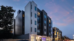 Ein mehrstöckiges Hotel mit modernem architektonischen Design, mit einem markanten Eckgebäude und einem Geschäft im Erdgeschoss.