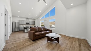 A spacious living area with a brown leather sofa, a white coffee table, and a kitchen in the background. - Two Bottles Inn - Palisade Wine Country Retreat Signature Suite Balcony 6 (Palisade)