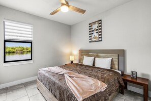 A bedroom with a bed, a nightstand, a ceiling fan, a window with blinds, and a wall clock. - Waterfront Paradise with Hot Tub, near 5th Ave (Cape Coral)