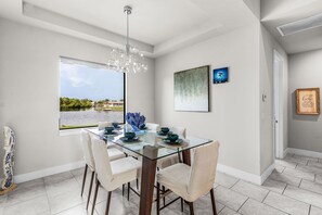 A dining area with a glass table, white chairs, a chandelier, and artwork on the walls. - Spacious Waterfront Home in Cape Coral with Private Boat Slip and Hot Tub (Cape Coral)