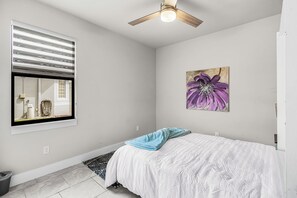 A bedroom with a bed, a ceiling fan, a window with blinds, a painting, and a small rug. - Spacious Waterfront Home in Cape Coral with Private Boat Slip and Hot Tub (Cape Coral)